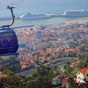 Cable car over coastal city with terra cotta roofs and cruise ships in the harbor. Cable Car is blue and high over the city.