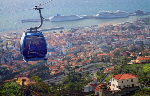 Cable car over coastal city with terra cotta roofs and cruise ships in the harbor. Cable Car is blue and high over the city.