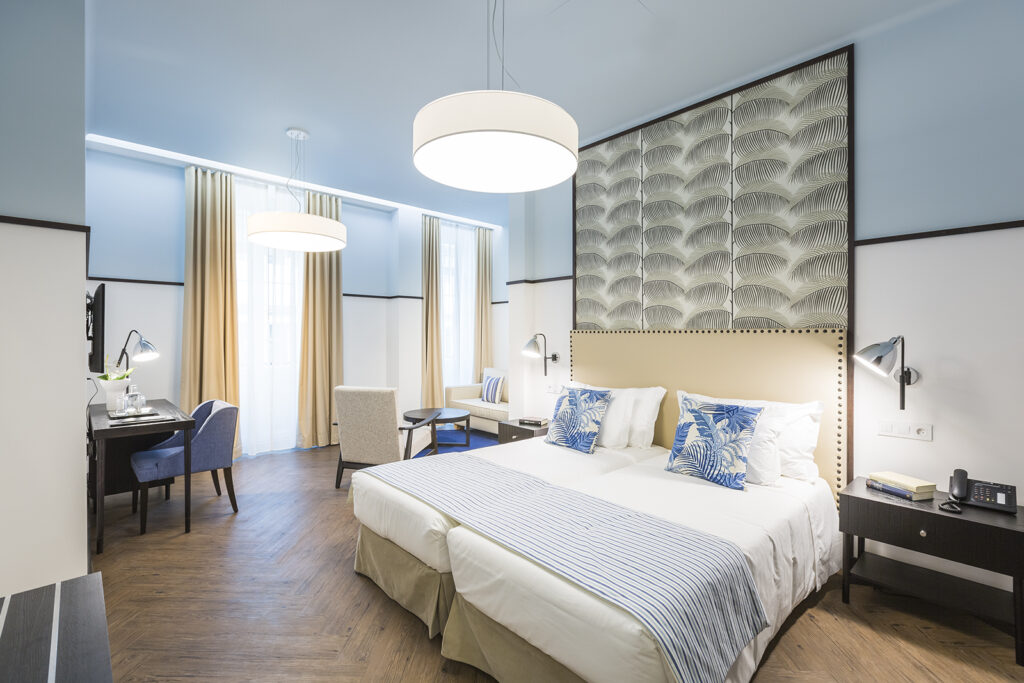 Bright and clean hotel room with light blue wall and two twin beds together to form one bed.